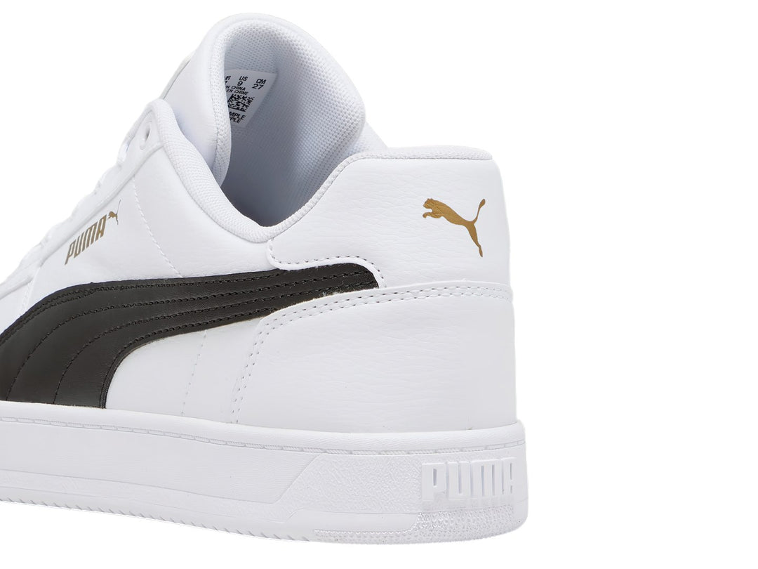 Tenis PUMA Caven 2.0 blancos con franja lateral negra y detalles dorados en la lengüeta.