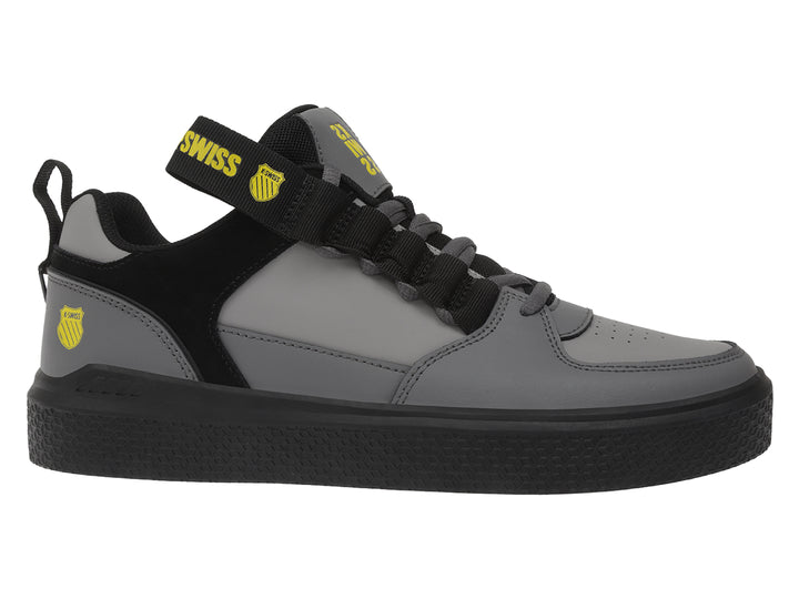 Tenis K-Swiss en color gris oscuro y negro con correa ajustable y suela negra.