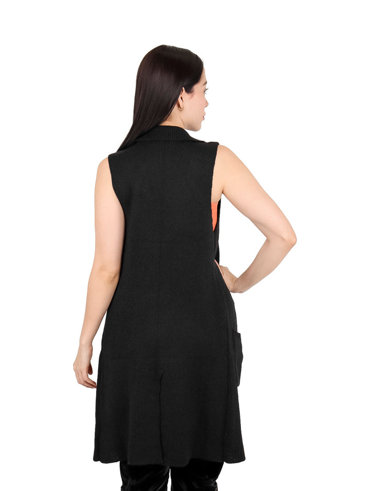 Mujer vistiendo un chaleco largo de color negro con botones, combinado con top naranja y pantalones negros.