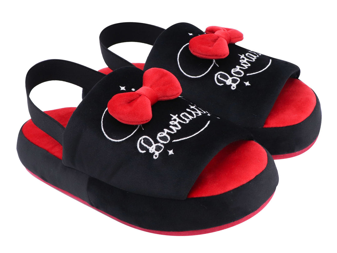 Par de pantuflas negras y rojas con un moño rojo decorativo y texto bordado en blanco.