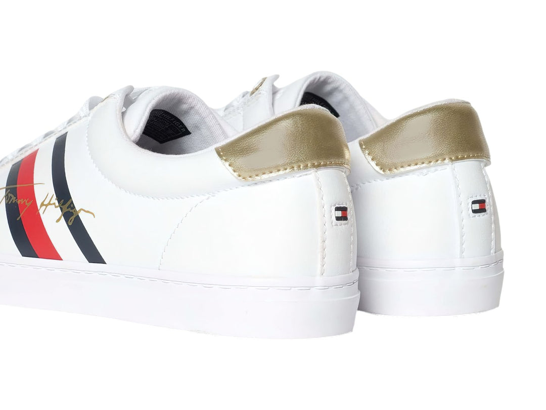 Tenis blancos de Tommy Hilfiger con detalle dorado en el talón y suela blanca.