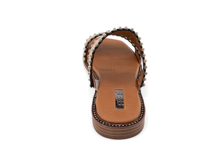 Sandalias slide color crudo con dos bandas decoradas con tachuelas y suela marrón.