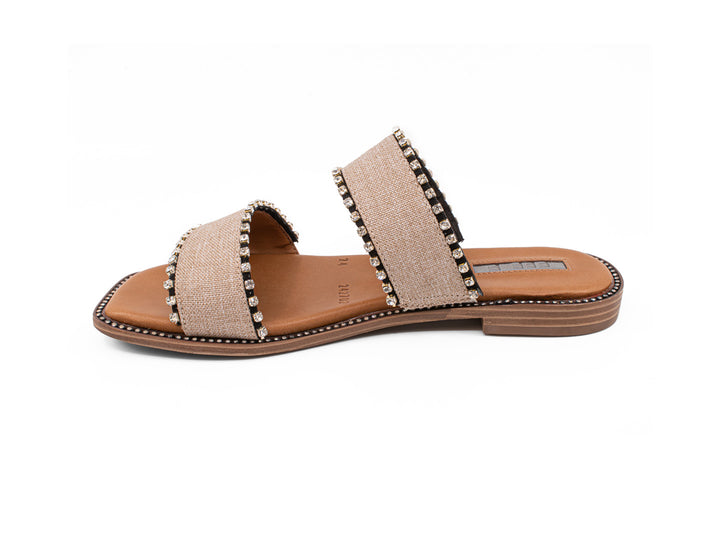 Sandalias slide color crudo con dos bandas decoradas con tachuelas y suela marrón.
