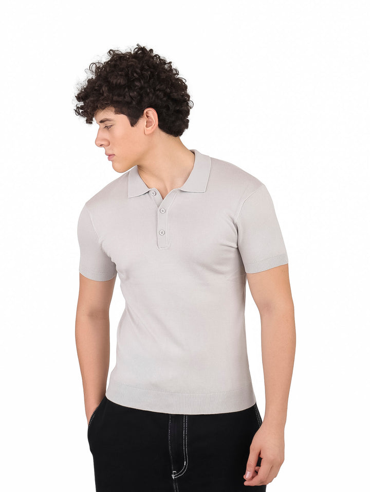 Hombre vistiendo playera polo tejida de color gris claro y pantalones negros.