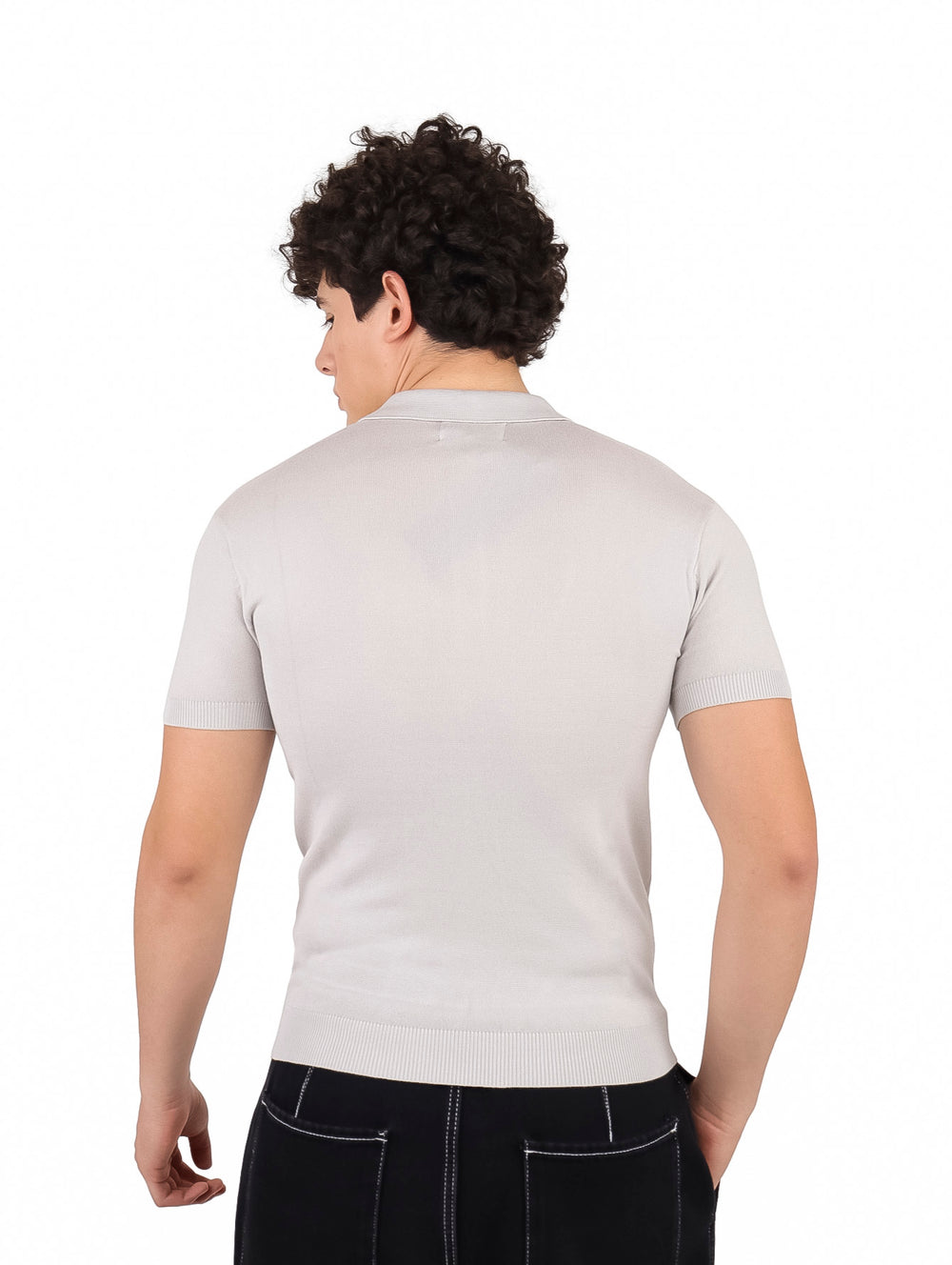 Hombre vistiendo playera polo tejida de color gris claro y pantalones negros.