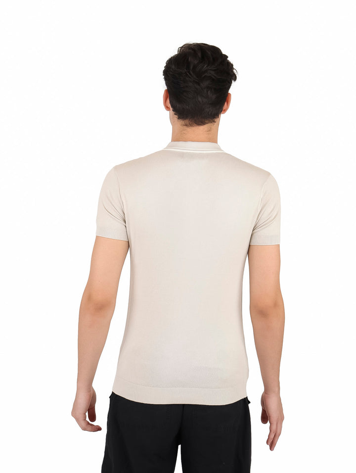 Hombre vistiendo playera polo tejida color arena con pantalones negros.