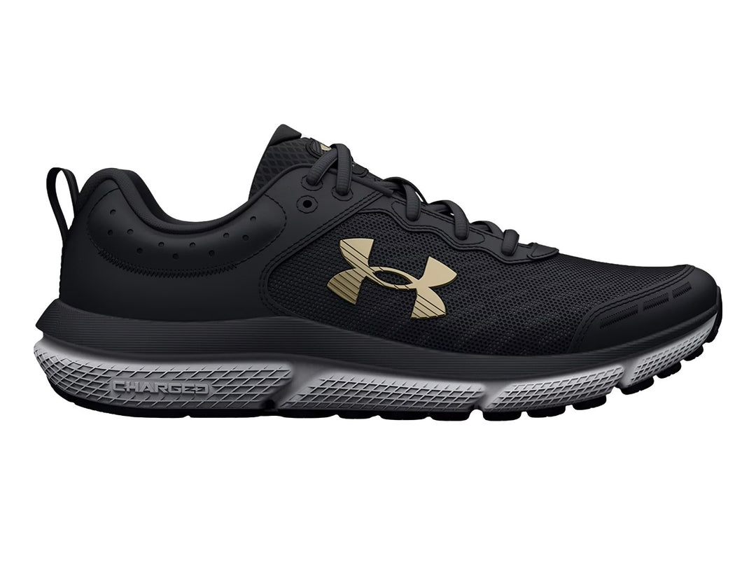Tenis deportivos Under Armour color negro con suela blanca y logo dorado para niños.