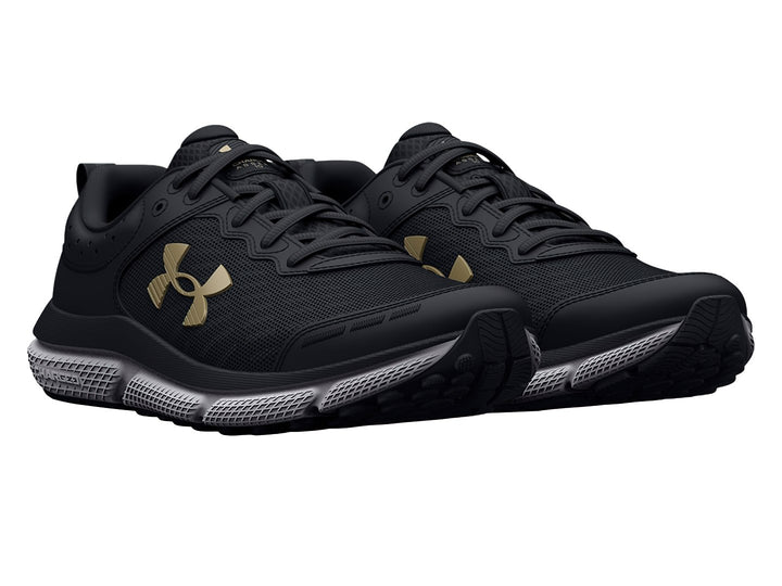 Tenis deportivos Under Armour color negro con suela blanca y logo dorado para niños.