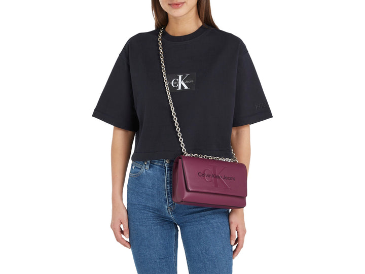 Bolso de hombro Calvin Klein Jeans color morado con correa de cadena plateada y logo en relieve.