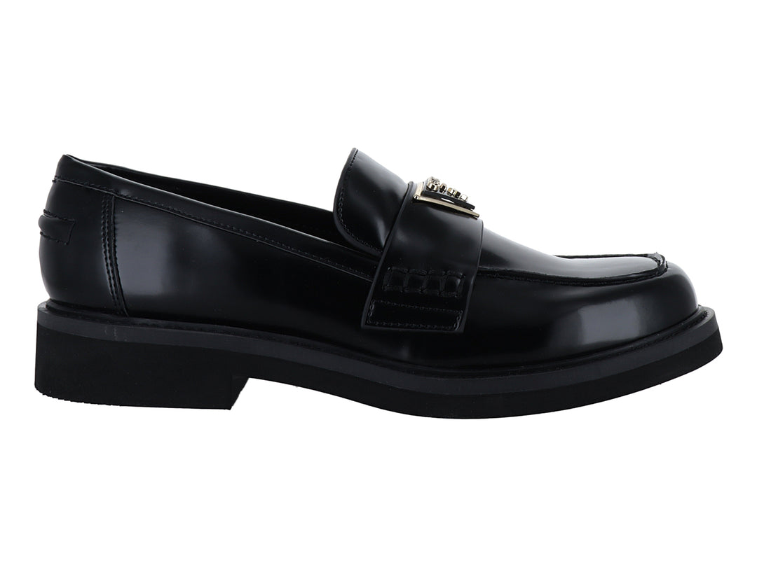 Zapato tipo mocasín Guess en color negro brillante con hebilla dorada y suela gruesa.