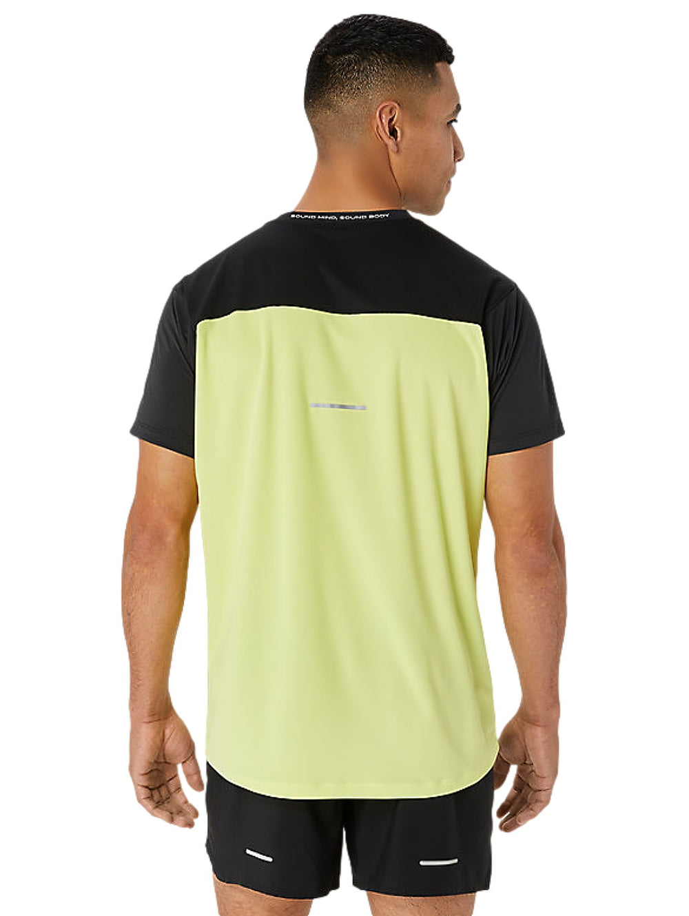 Hombre vistiendo camiseta deportiva ASICS en colores negro y amarillo brillante con shorts negros.