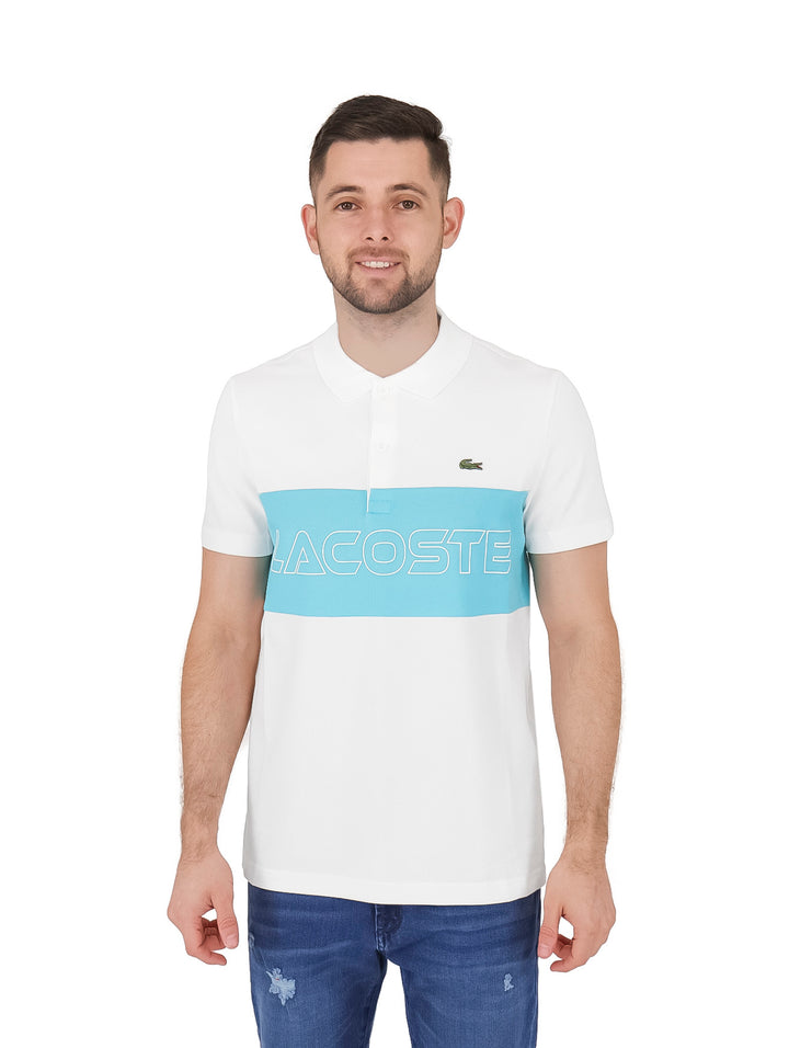 Hombre vistiendo polo Lacoste blanco con franja azul celeste y letras grandes en el pecho