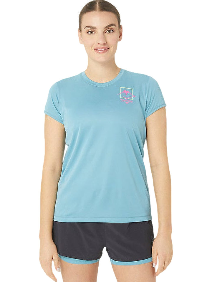 Mujer vistiendo camiseta deportiva ASICS de color azul grisáceo con logo en el pecho y shorts oscuros.