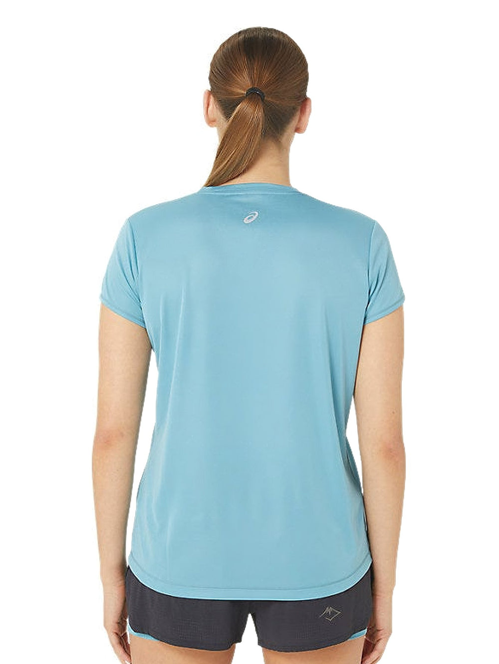 Mujer vistiendo camiseta deportiva ASICS de color azul grisáceo con logo en el pecho y shorts oscuros.