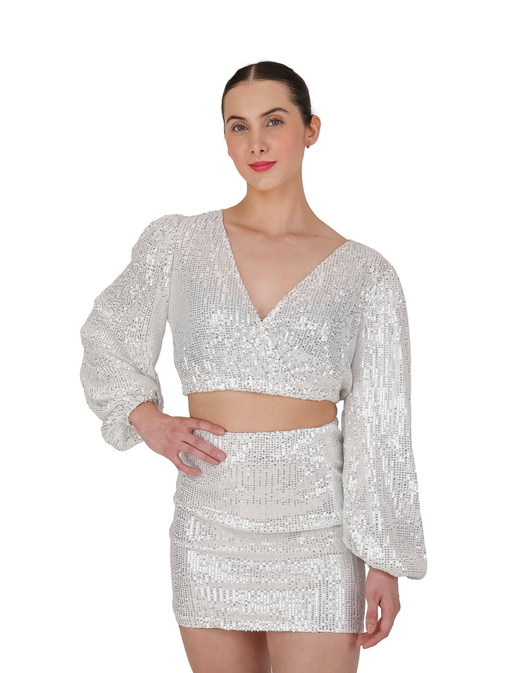 Conjunto de blusa crop top y minifalda color ivory con lentejuelas brillantes y mangas largas acampanadas para mujer.
