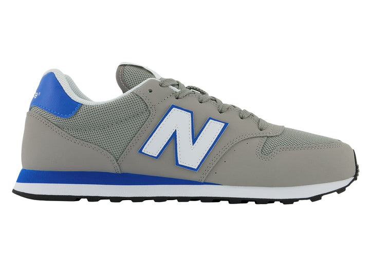 Tenis New Balance color gris con detalles en azul, suela blanca y negra.