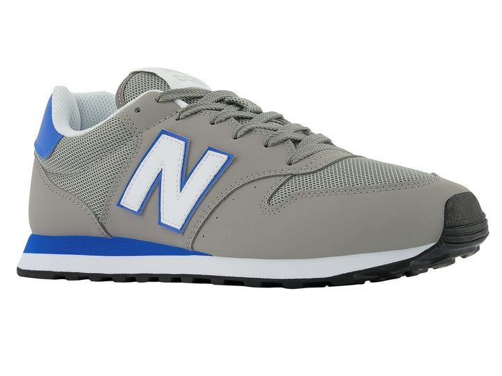 Tenis New Balance color gris con detalles en azul, suela blanca y negra.