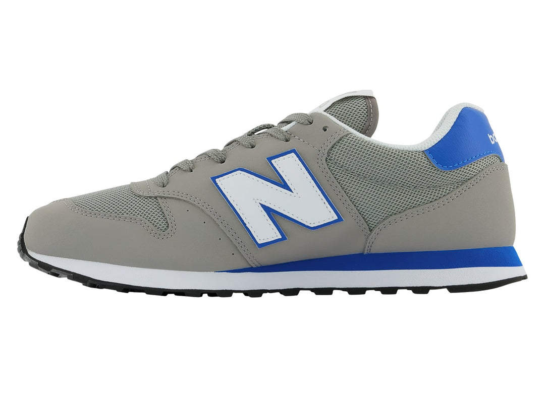 Tenis New Balance color gris con detalles en azul, suela blanca y negra.