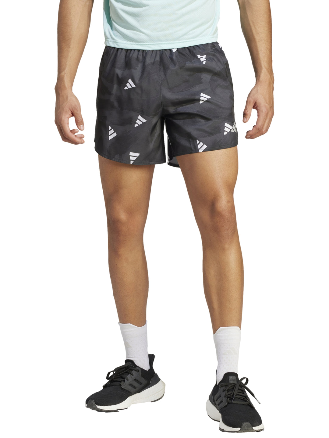 Hombre vistiendo shorts deportivos Adidas color negro con estampado de logos blancos.