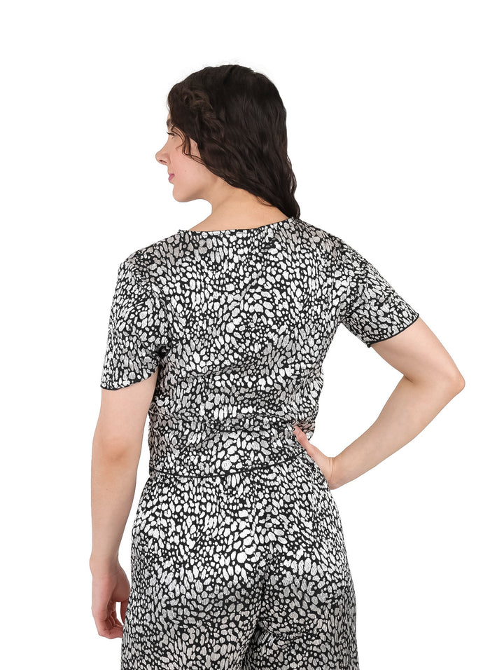 Mujer vistiendo blusa de manga corta con estampado abstracto en color plata y negro brillante.