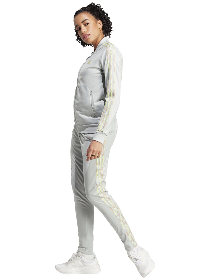 Mujer vistiendo pantalones deportivos Adidas color plata con franjas laterales multicolores.