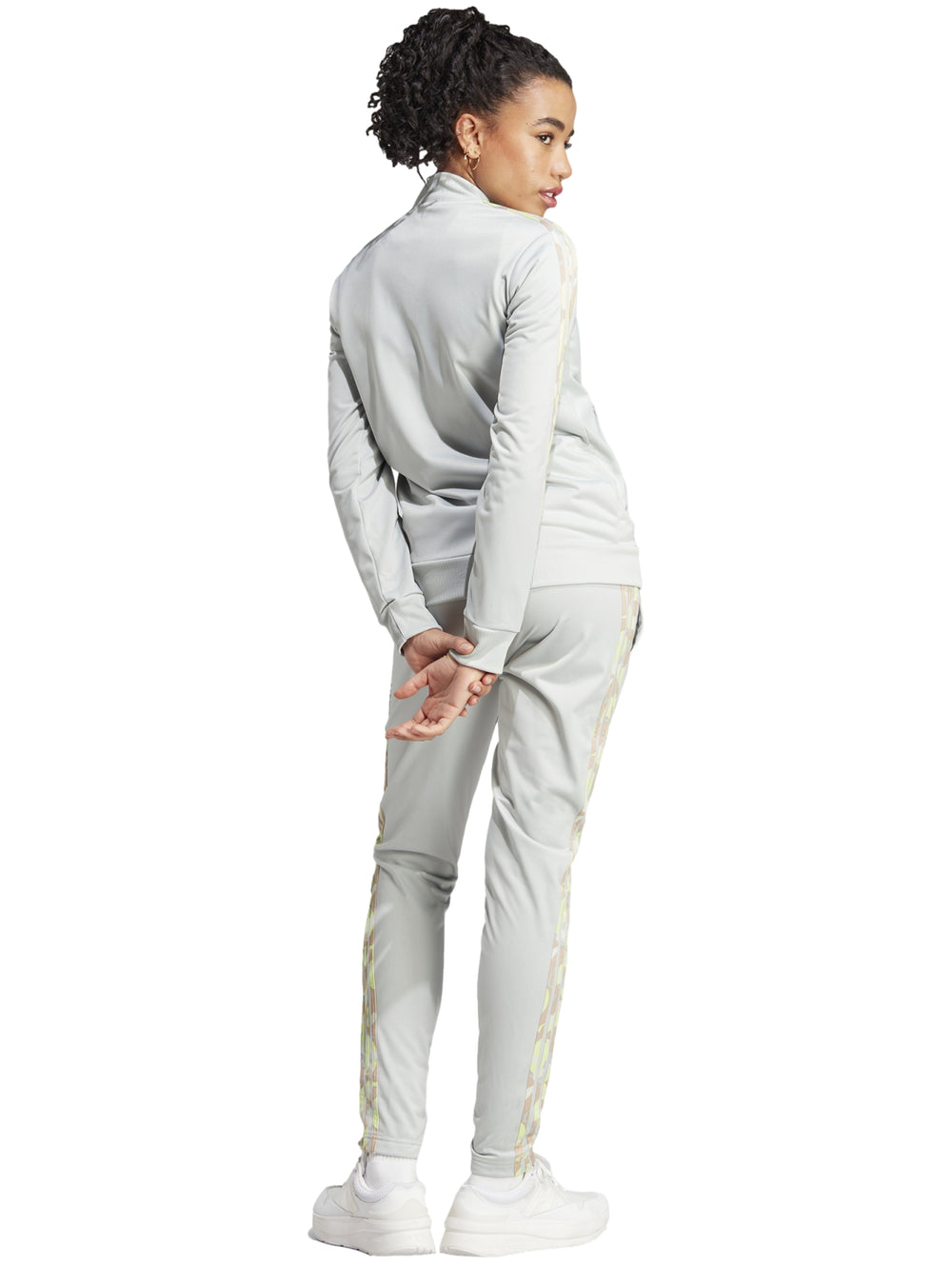 Mujer vistiendo pantalones deportivos Adidas color plata con franjas laterales multicolores.