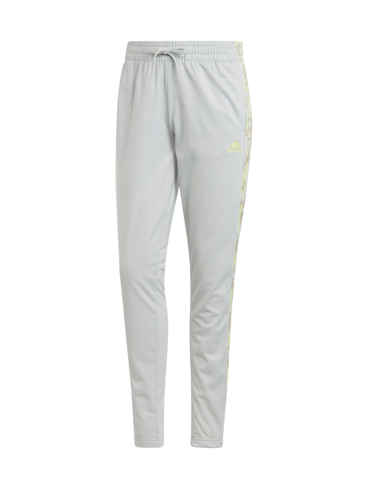 Mujer vistiendo pantalones deportivos Adidas color plata con franjas laterales multicolores.