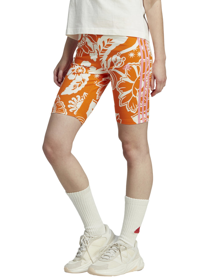 Shorts deportivos Adidas color naranja con estampado floral blanco y rayas laterales blancas.