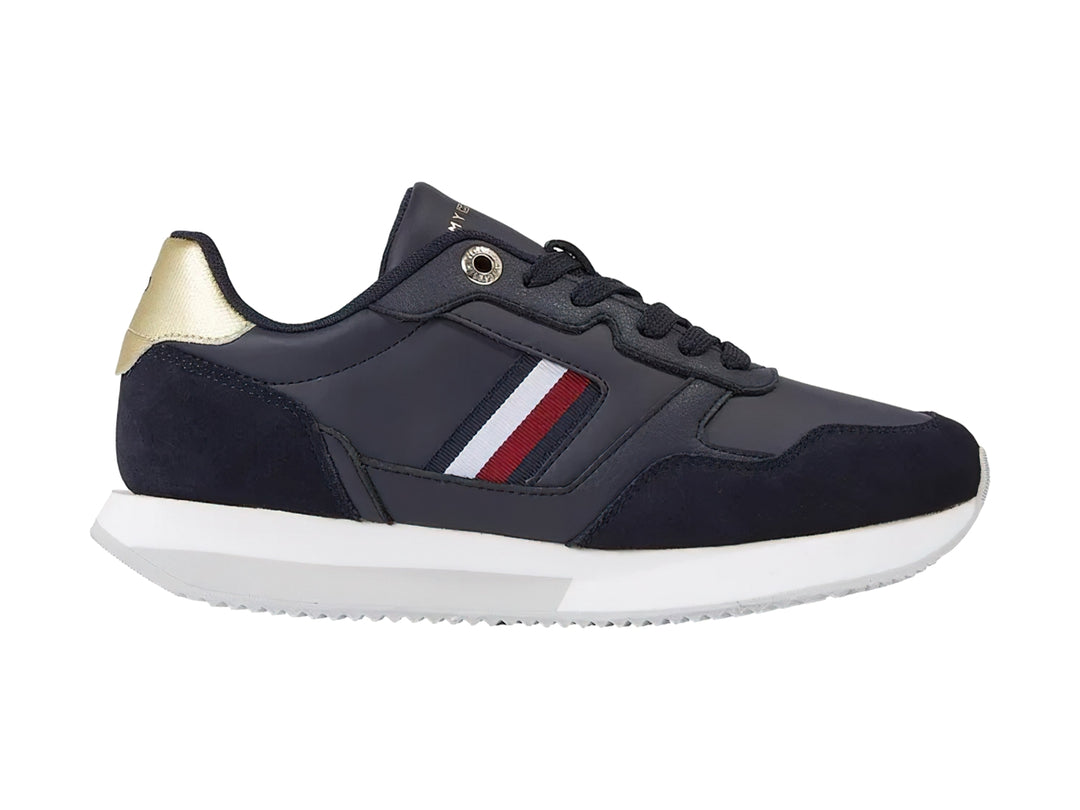 Tenis Tommy Hilfiger azul marino con suela blanca, detalles dorados en el talón y rayas laterales.