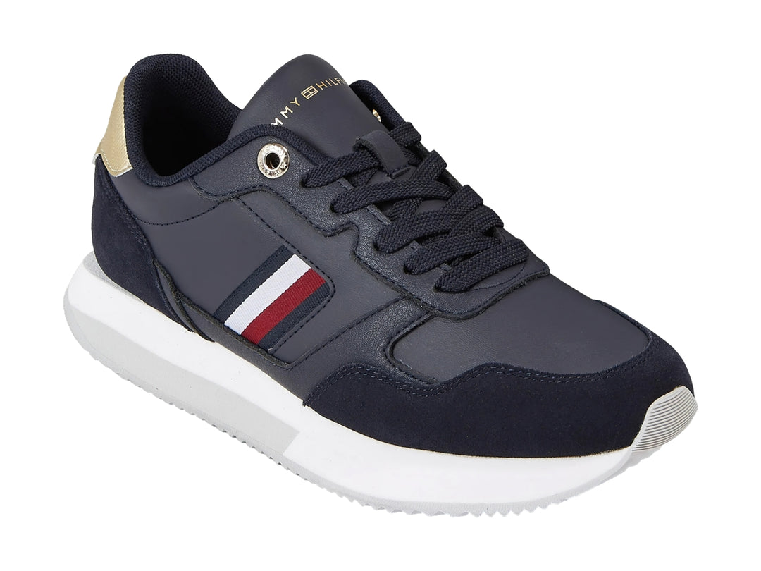 Tenis Tommy Hilfiger azul marino con suela blanca, detalles dorados en el talón y rayas laterales.
