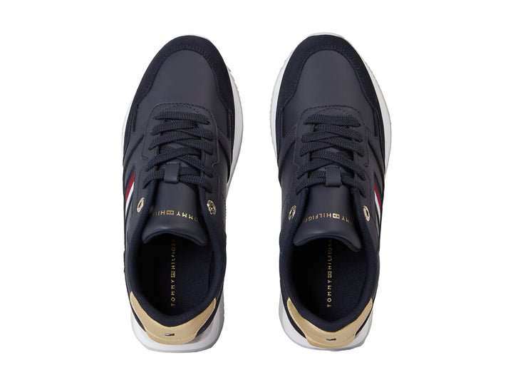 Tenis Tommy Hilfiger azul marino con suela blanca, detalles dorados en el talón y rayas laterales.