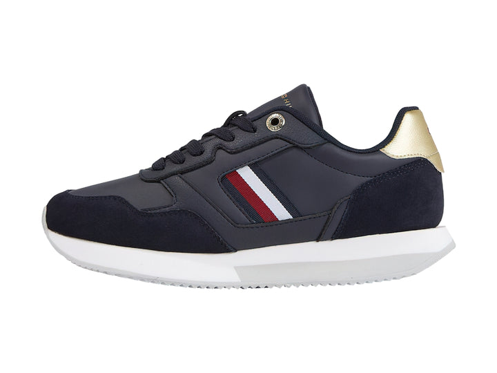 Tenis Tommy Hilfiger azul marino con suela blanca, detalles dorados en el talón y rayas laterales.