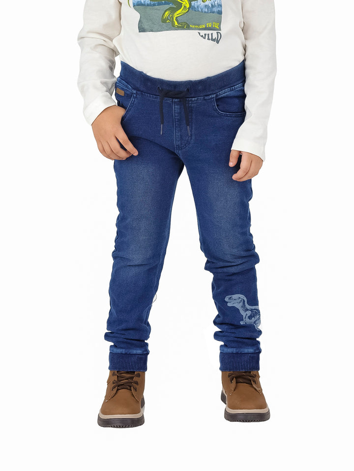 Pantalón denim azul para niño con cintura elástica y detalle de dinosaurio en la pierna.