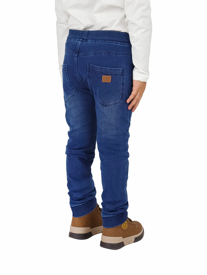 Pantalón denim azul para niño con cintura elástica y detalle de dinosaurio en la pierna.