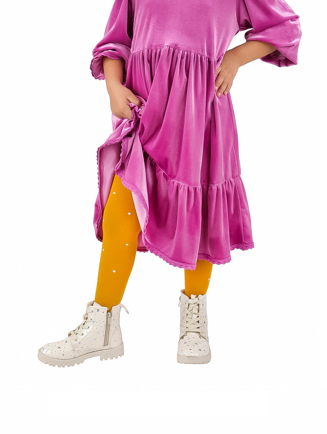 Niña vistiendo leotardo color mostaza con puntos blancos, vestido morado y botas blancas.