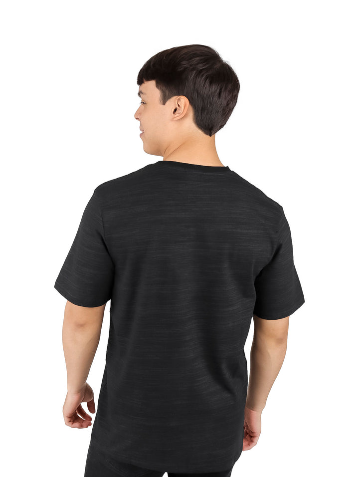 Hombre vistiendo una camiseta de manga corta color negro con un pequeño detalle circular naranja en el pecho.