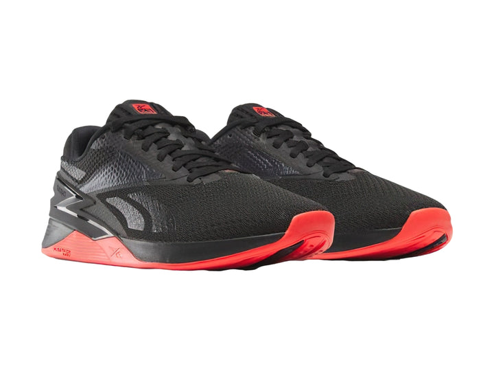 Tenis deportivos Reebok Nano X3 color negro con suela en tono rojo neón.