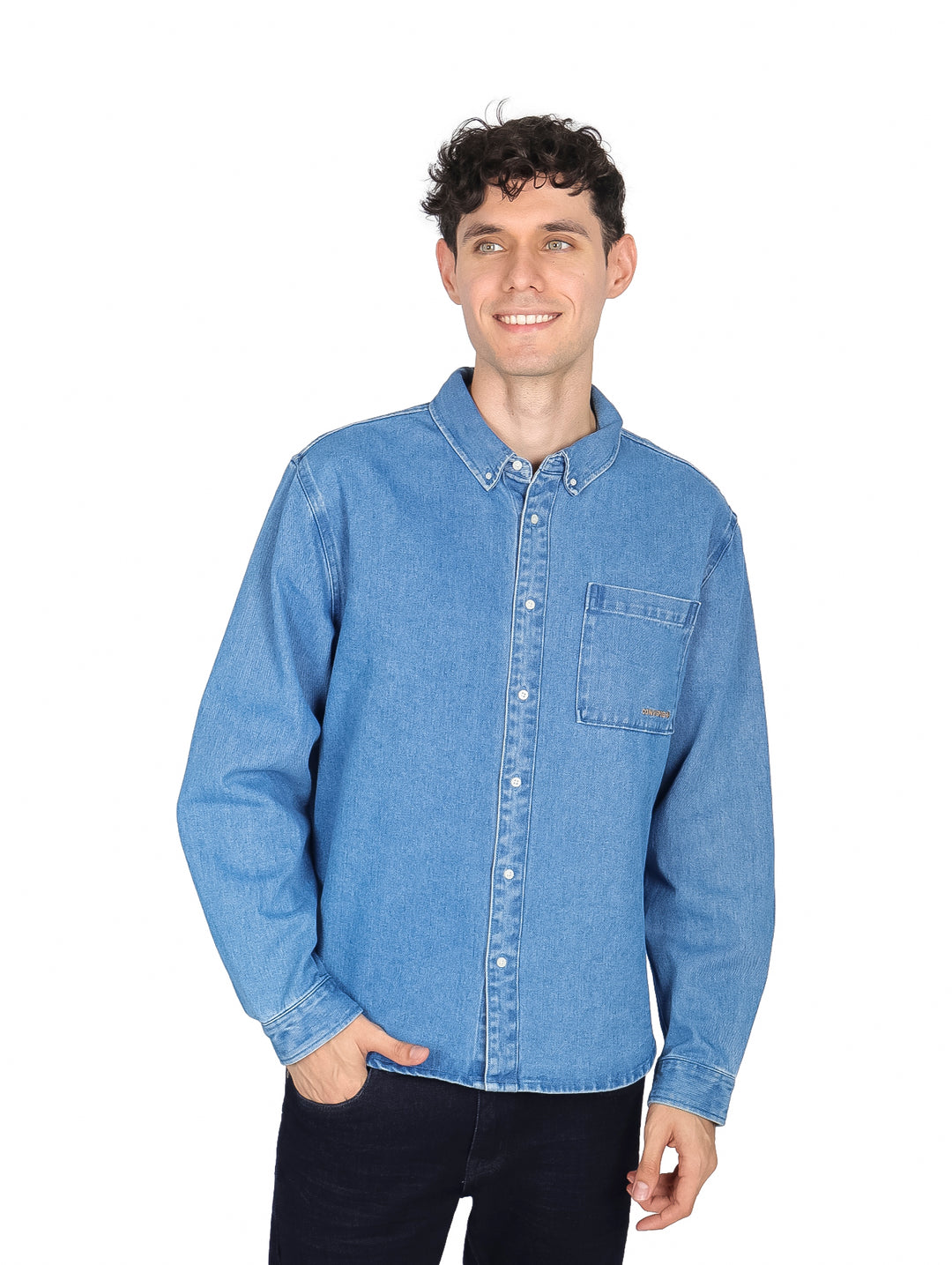 Hombre vistiendo una camisa de mezclilla azul claro de manga larga con botones y bolsillo frontal.