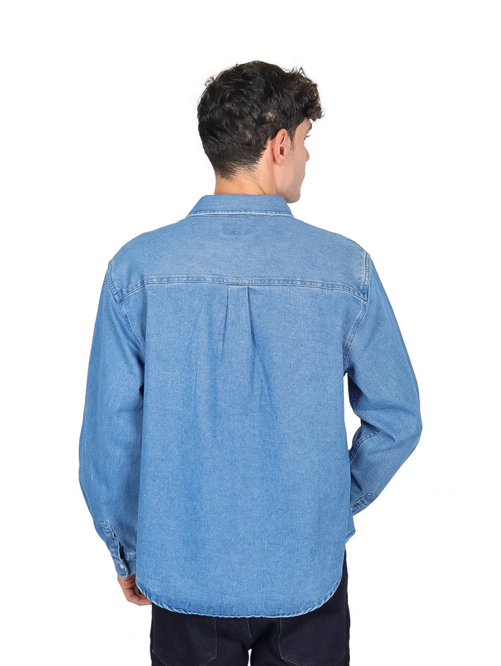 Hombre vistiendo una camisa de mezclilla azul claro de manga larga con botones y bolsillo frontal.