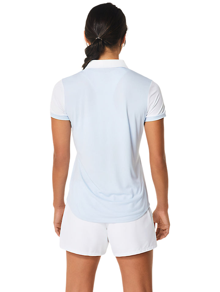 Mujer vistiendo polo deportivo ASICS color celeste y blanco con shorts blancos.