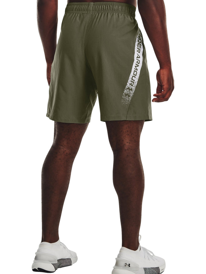 Hombre vistiendo shorts deportivos de color verde oliva de la marca Under Armour.