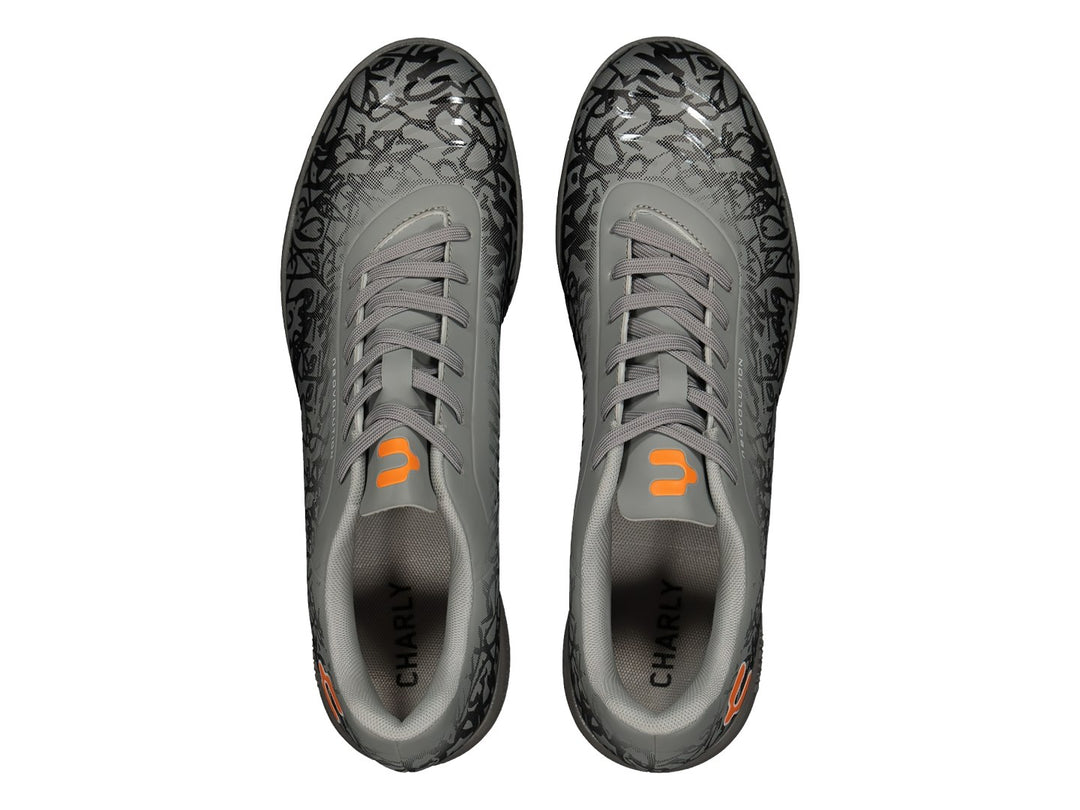 Zapato de fútbol Charly color gris con patrones negros y detalles en naranja, suela para turf.