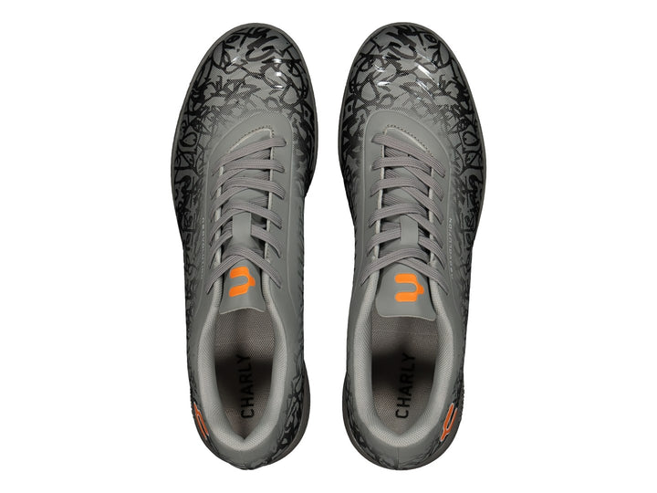 Zapato de fútbol Charly color gris con patrones negros y detalles en naranja, suela para turf.