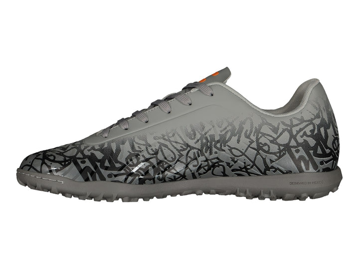 Zapato de fútbol Charly color gris con patrones negros y detalles en naranja, suela para turf.