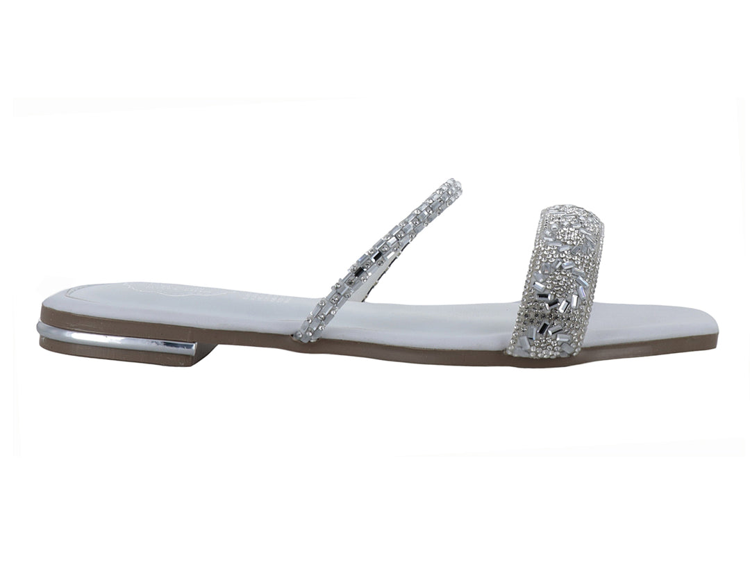 Sandalia plana blanca para niña con tiras decoradas con pedrería brillante plateada.