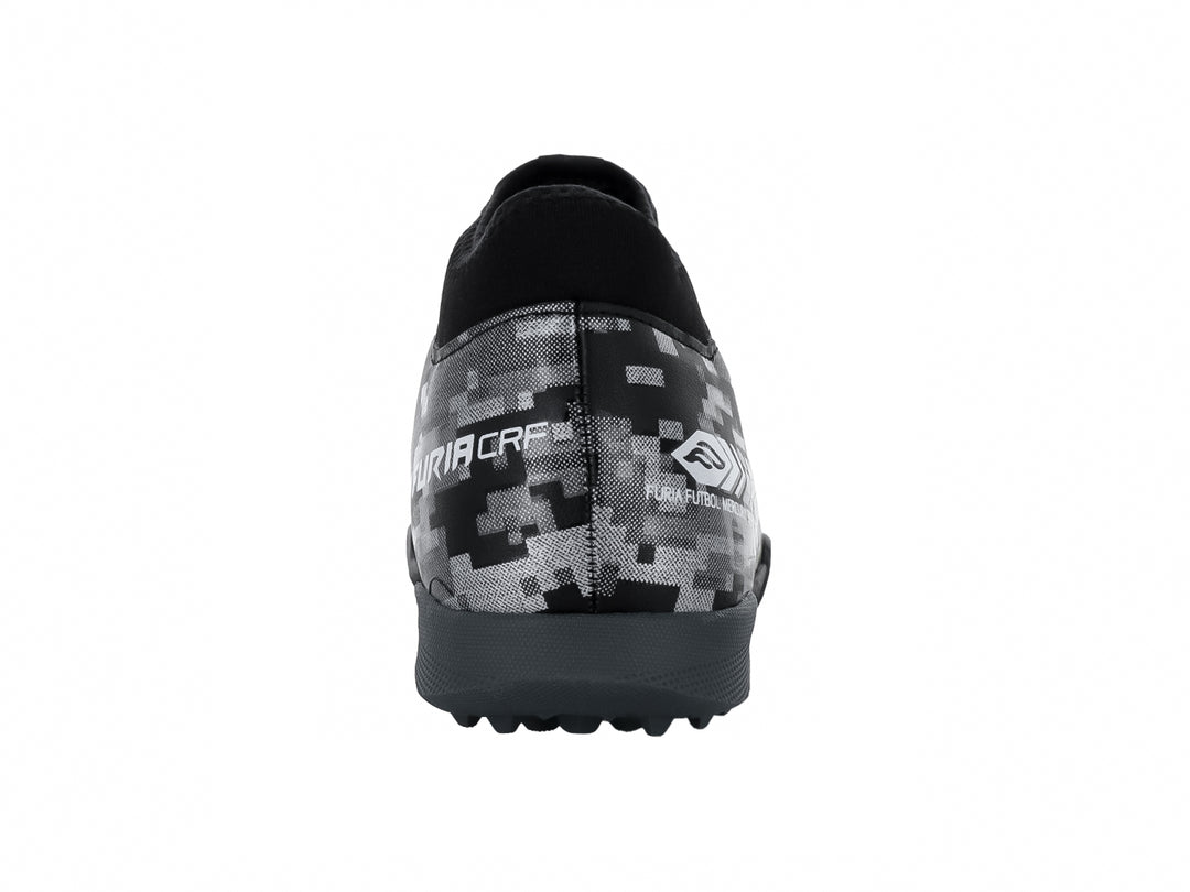 Calzado de fútbol Furia para niños en color negro y plata con patrón pixelado y suela para césped sintético.