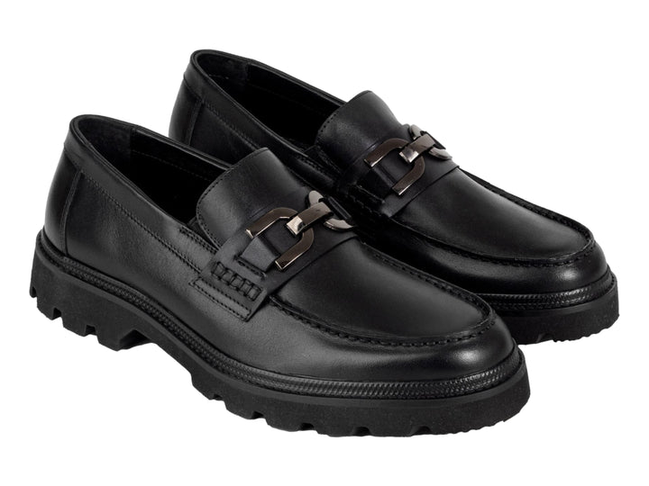 Zapato mocasín negro con suela track gruesa y detalle metálico en la parte superior.