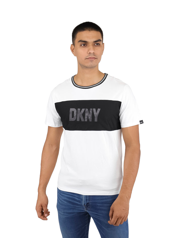 Hombre vistiendo camiseta blanca DKNY con panel horizontal negro en el pecho y cuello contrastado.