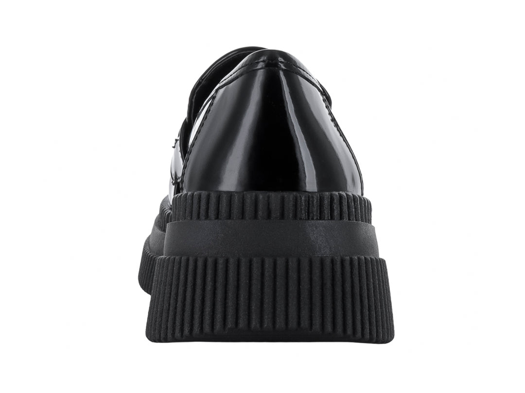 Zapato mocasín negro de acabado brillante con suela de plataforma gruesa y detalle metálico en la parte superior.