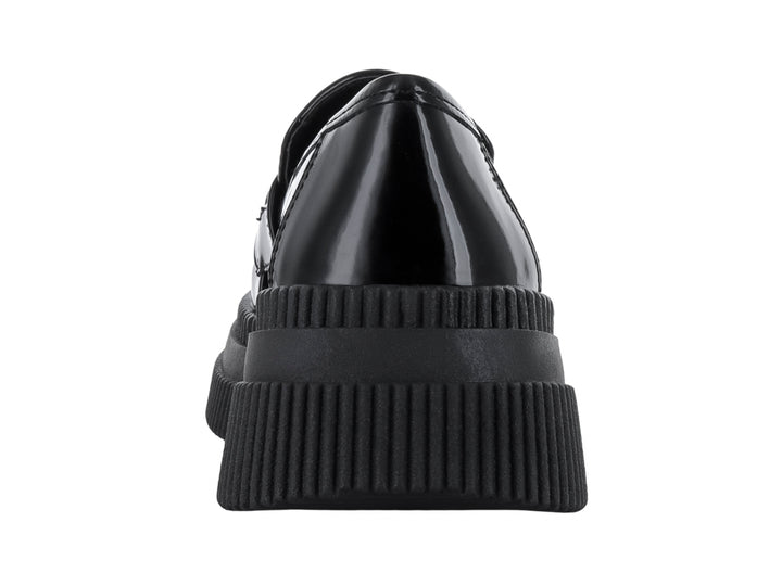 Zapato mocasín negro de acabado brillante con suela de plataforma gruesa y detalle metálico en la parte superior.